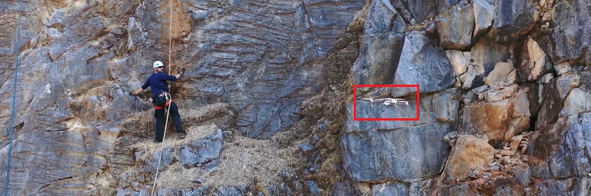 Search and rescue drone hovers to evaluate a rock climber trapped on a mountain face during a rescue mission.