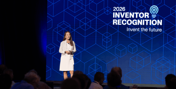 Speaker presenting at WD Elevate 2026 on stage in front of large display screen showing "2026 Inventor Recognition – Invent the future" messaging and geometric design.