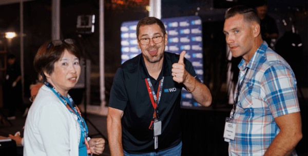 Three WD employees networking and conversing at WD Elevate event, with center figure giving thumbs up gesture in casual celebration moment.