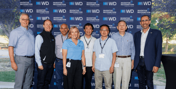 Eight WD employees and leaders posing together at WD Elevate event in front of WD Inventor Recognition branded backdrop.
